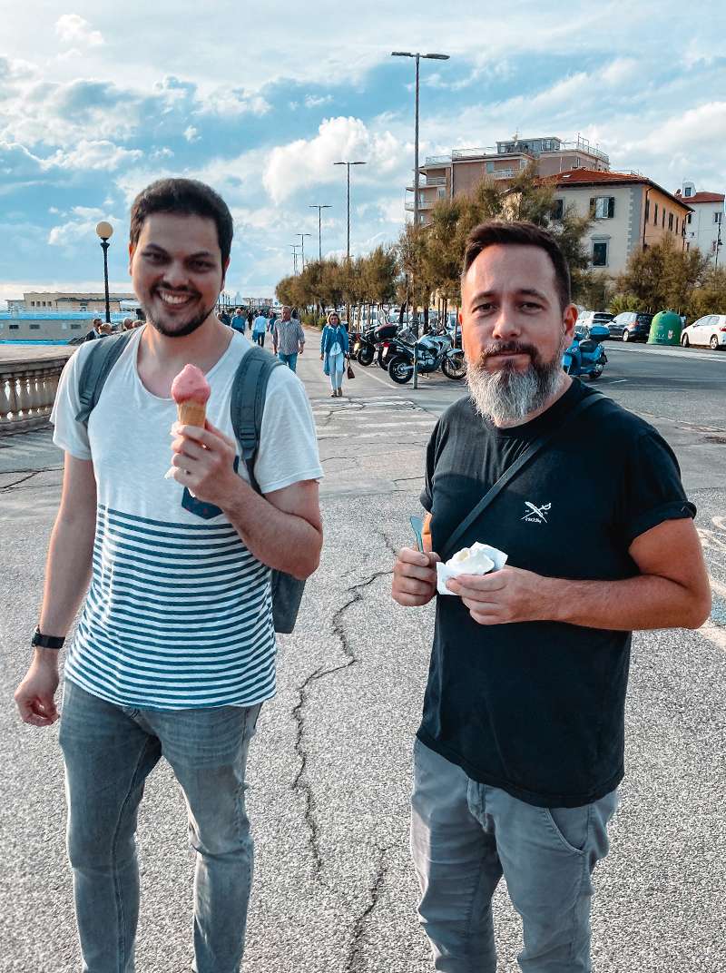 Amadeus und Arne stehen gemeinsam an einer Meerespromenade und essen ein Eis.