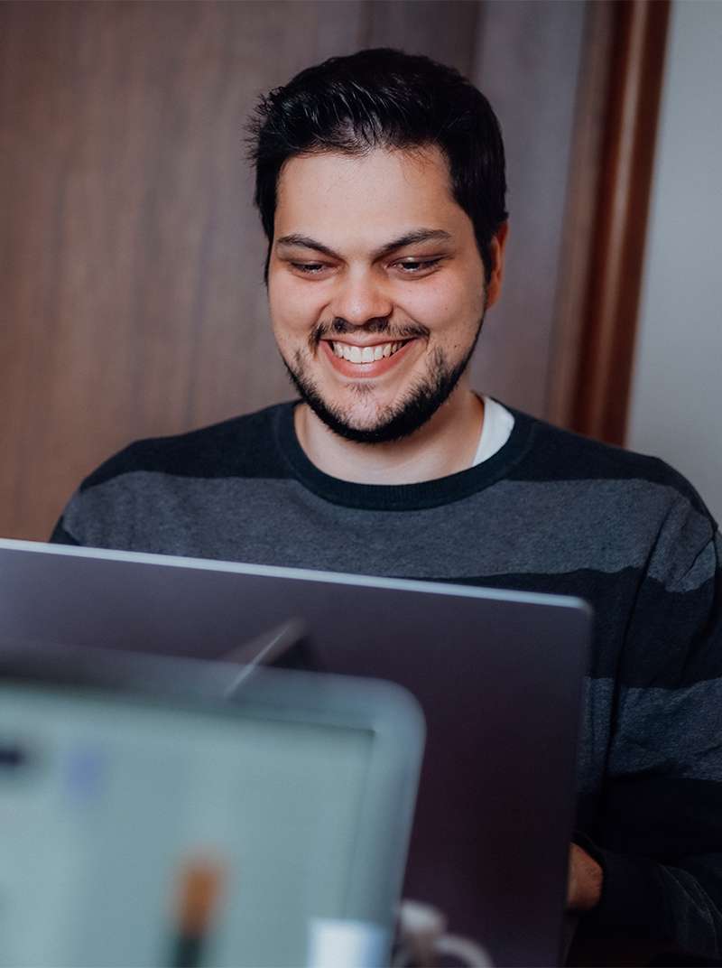 Amadeus sitzt lachend hinter seinem Macbook.