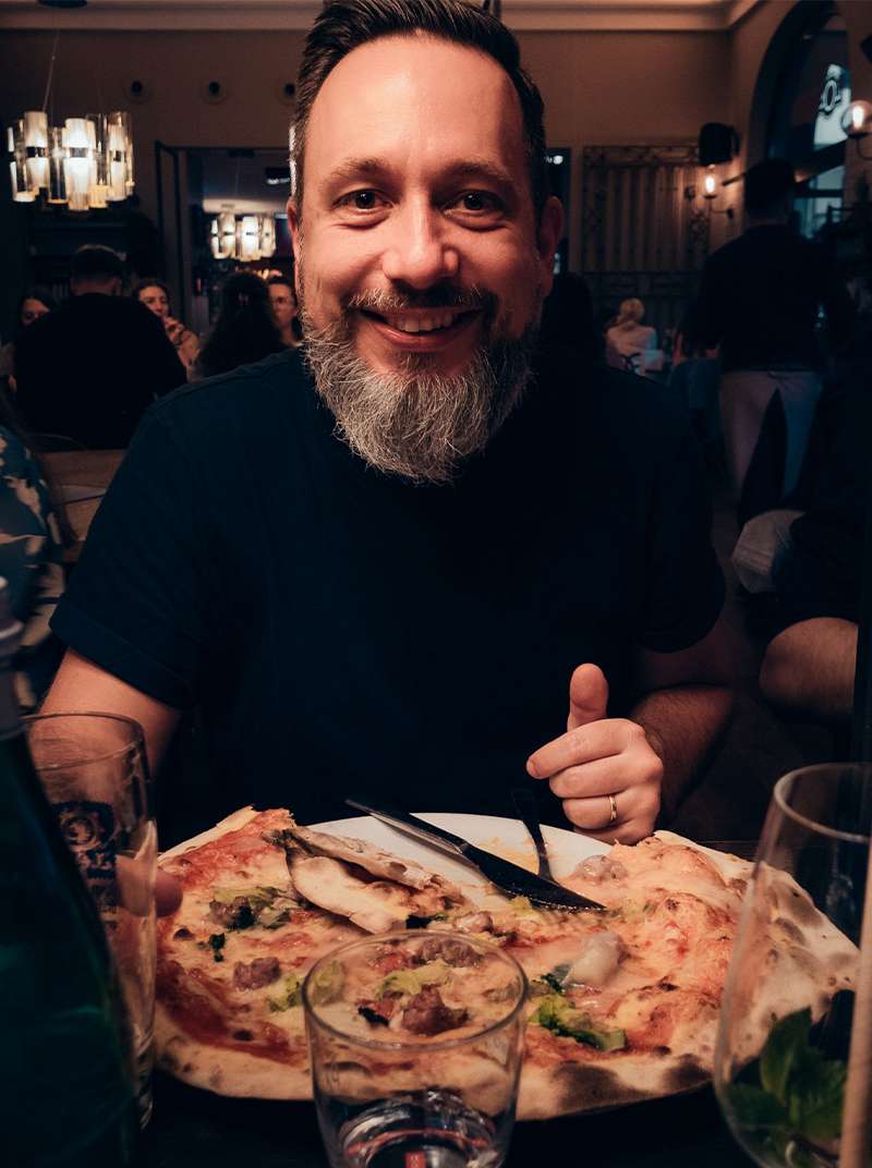 Arne sitzt lachend vor einem großen Teller mit Pizza.