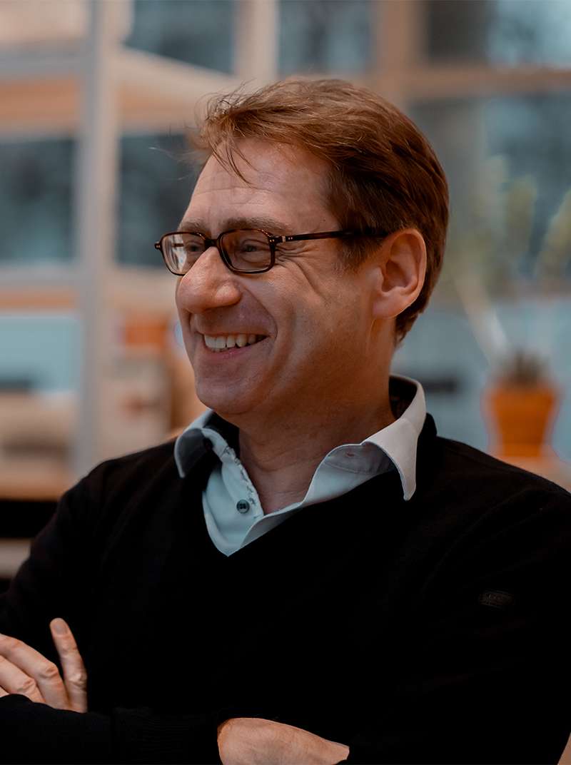 Lothar sitzt lachend im Coworking-Space und hat die Arme vor der Brust verschränkt.