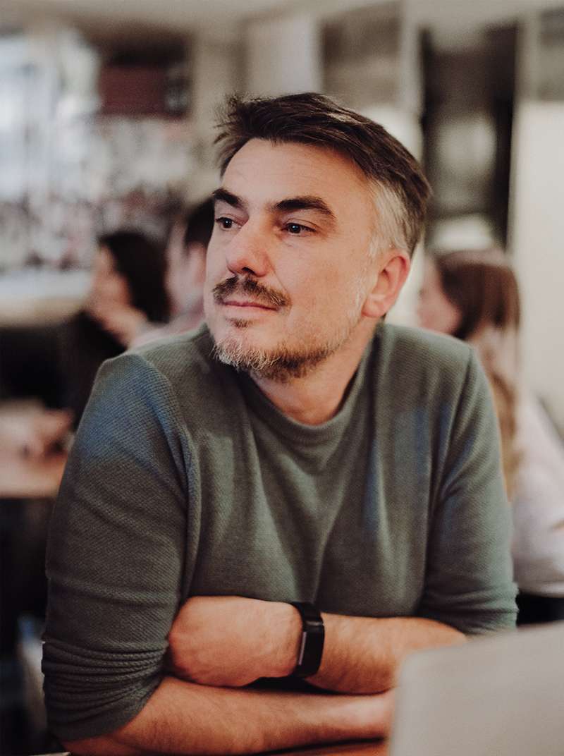 Max sitzt in einem belebten Restaurant und blickt zur Seite